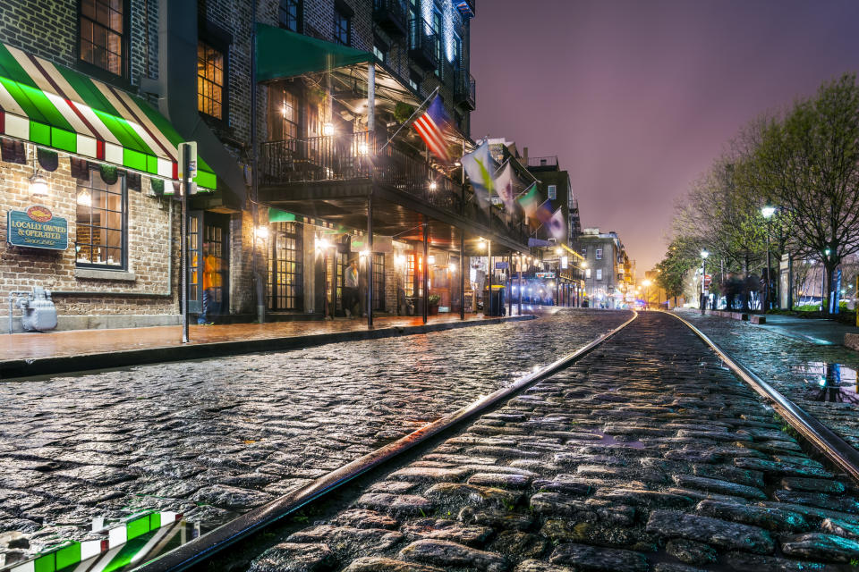 Cobblestone street at night with lit storefronts and iron balconies