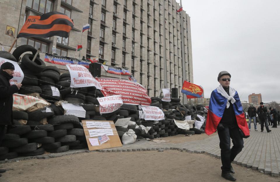 A pro-Russian activist with a Russian flag pass by a barricade at a regional administration building that they had seized earlier in Donetsk, Ukraine, in Donetsk, Ukraine, Friday, April 11, 2014. Ukraine’s prime minister on Friday told leaders in the country’s restive east that he is committed to allowing regions to have more powers. Yatsenyuk Friday morning flew into Donetsk, where pro-Russian separatists are occupying the regional administration building and calling for a referendum that could prefigure seeking annexation by Russia. (AP Photo/Efrem Lukatsky)