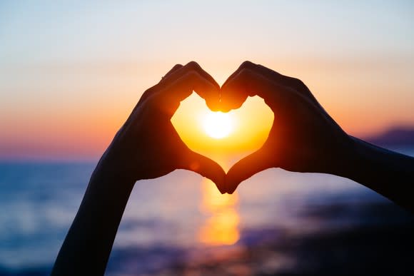 Fingers forming a heart shape with a sunset in the background