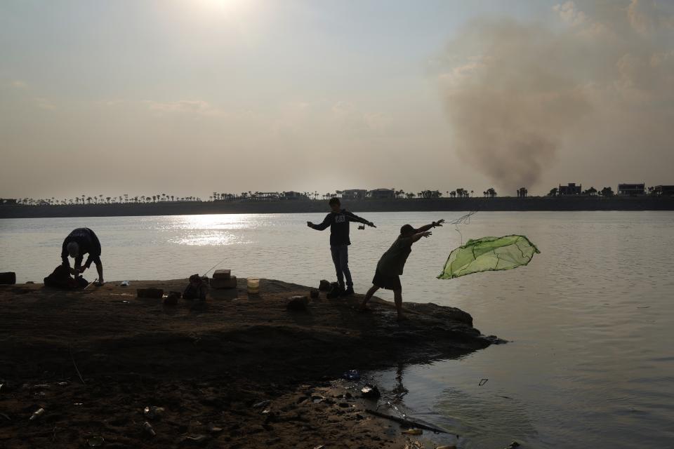 People fish on the exposed bed of the Paraguay river, as a column of smoke rises on the other shore, amid a historic drought that is affecting the river´s level, in Mariano Roque Alonso, Paraguay, Monday, Sept. 20, 2021. (AP Photo/Jorge Saenz)