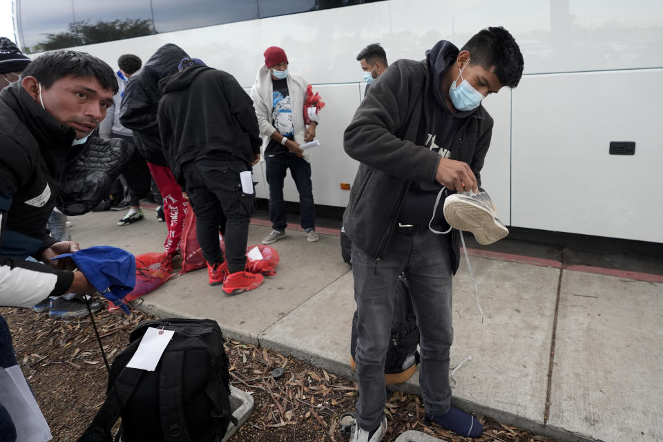 Migrants unload their items off a bus as they arrive at a bus stop after leaving a processing facility, Friday, Feb. 23, 2024, in San Diego. Hundreds of migrants were dropped off Friday at a sidewalk bus stop amid office parks in San Diego with notices to appear in immigration court after local government funding for a reception center ran out of money sooner than expected. (AP Photo/Gregory Bull)