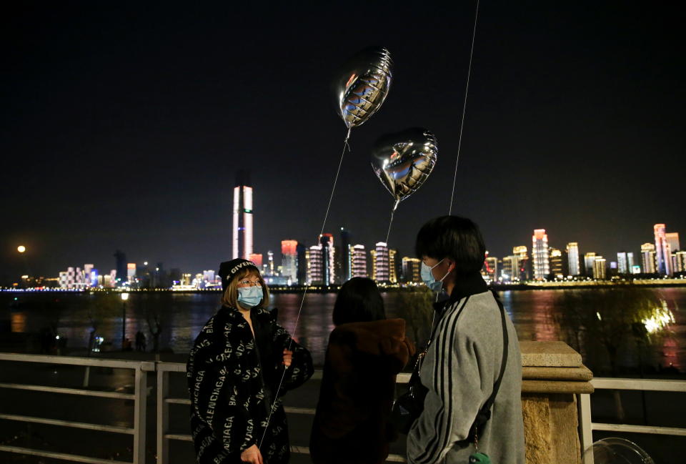 People wearing masks hold balloons by a river on New Year's Eve in Wuhan. (Reuters)