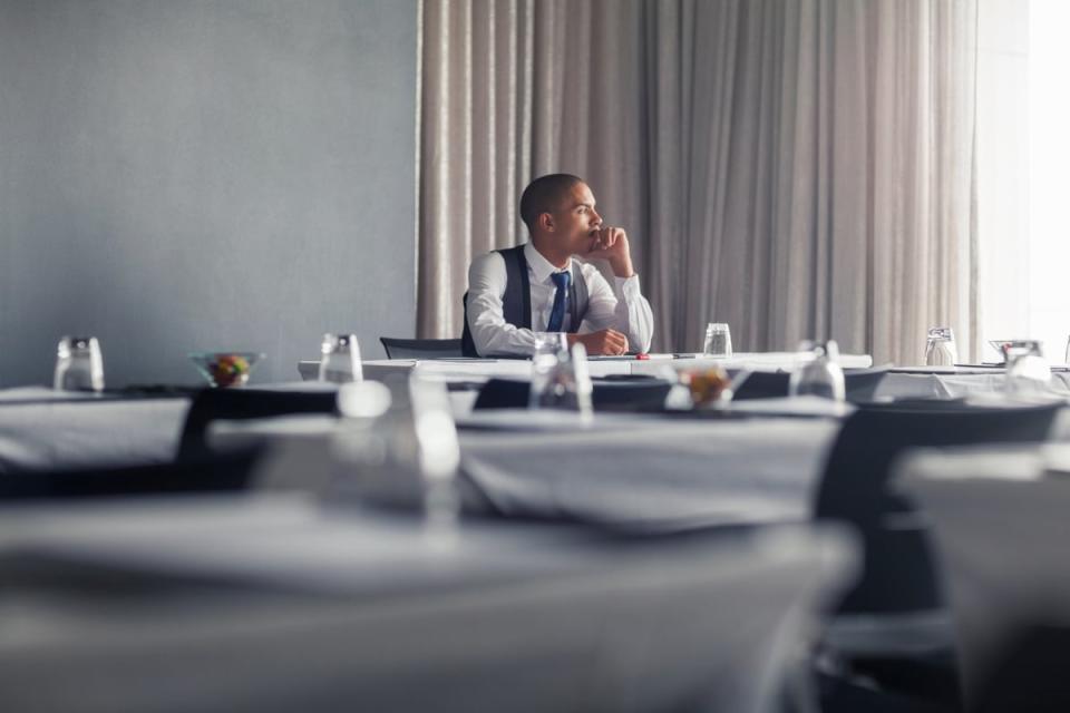 A person wearing professional attire sits at a table alone and stares out a window. 