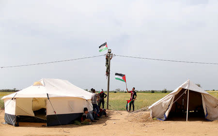 A man hangs a Palestinian flag at an electric pole near the border with Israel, in the southern Gaza Strip March 28, 2018. REUTERS/Ibraheem Abu Mustafa