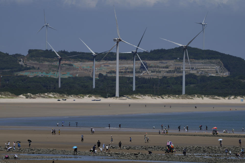 FILE - Beachgoers walk near wind turbines along the coast of Pingtan in Southern China's Fujian province, on Aug. 6, 2022. China announced ambitious schemes to enable the country to meet its 2030 clean energy goals five years ahead of schedule. (AP Photo/Ng Han Guan, File)
