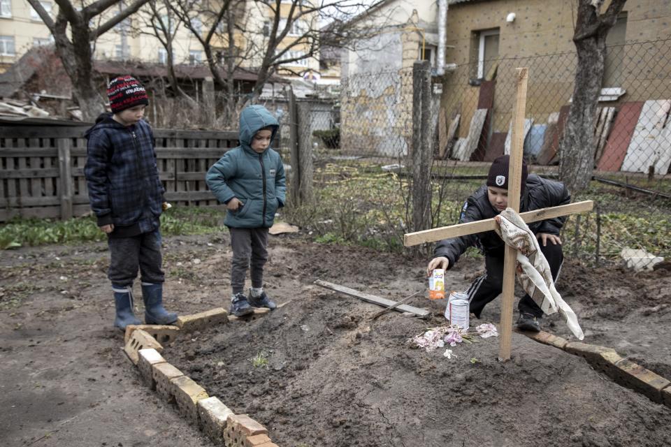 A young kid gives an offering of food to his mother grave as his younger brother and a neighbor stand next to it, in the town of Bucha, on the outskirts of Kyiv, after the Ukrainian army secured the area following the withdrawal of the Russian army from the Kyiv region on previous days, Bucha, Ukraine, April 4th, 2022.