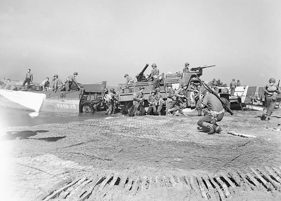 U.S. troops bring artillery ashore at Salerno, Italy, in September 1943. The military policeman in the foreground ducks from a nearby German shell hit.