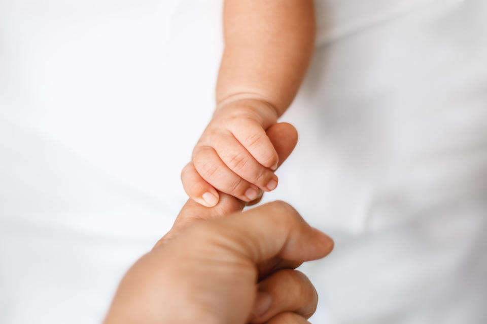 A baby holds their parent's finger