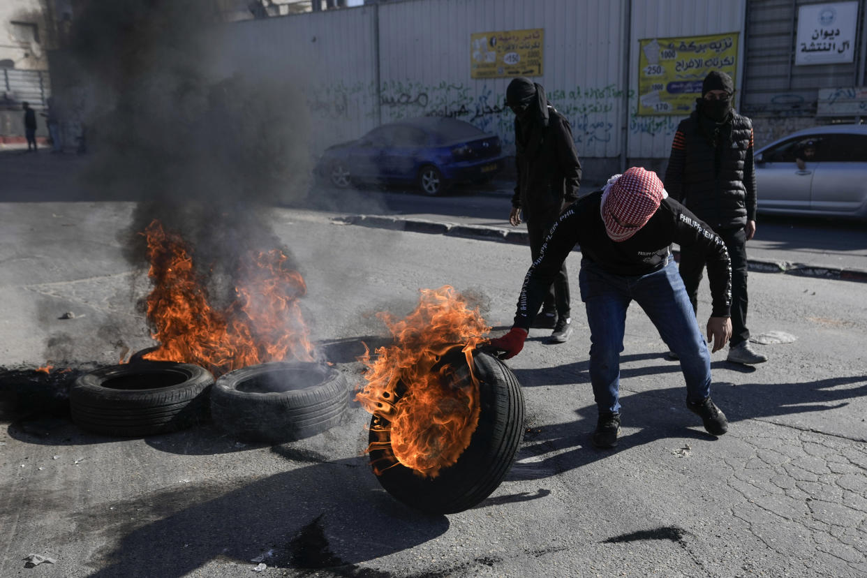 Masked Palestinian demonstrators burn tires in a protest against a deadly Israeli army raid after the funeral of Yusef Muhaisen in the West Bank town of al Ram, north of Jerusalem, Friday, Jan. 27, 2023. Muhaisen, 22, was killed during clashes with Israeli troops. (AP Photo/Majdi Mohammed)