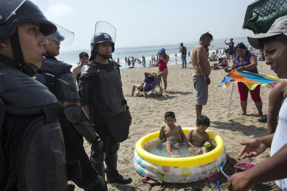 En esta imagen, tomada el 15 de febrero de 2020, dos niños dentro de una piscina hinchable comen manzanas cubiertas de azúcar mientras policías se disponen a retirar de la playa a un vendedor ambulante sin licencia, en Agua Dulce, Lima, Perú. (AP Foto/Rodrigo Abd)