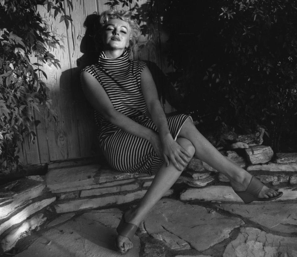 Marilyn Monroe (1926 - 1962) sits in shadow against a garden fence, 1954