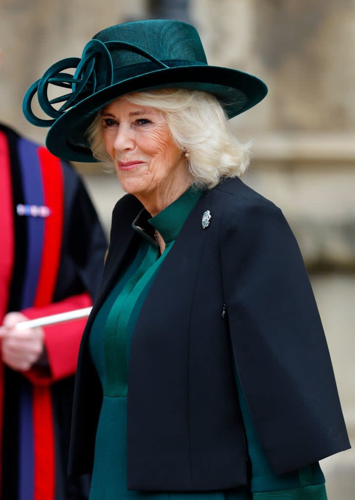 Camilla, Queen Consort, at an event, wearing a wide-brimmed hat and coat with a brooch