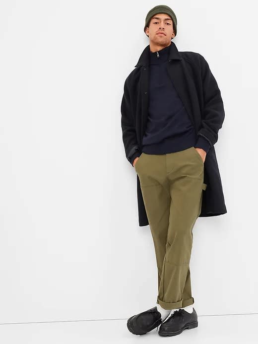 black long front button coat worn open over a sweater and green pants