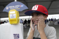 Niko Anastasopoulos, 6, of Upper Saddle River, N.J., applies sunscreen from a dispenser at the New York Giants NFL football training camp, Thursday, Aug. 2, 2018, in East Rutherford, N.J. The NFL and American Cancer Society teamed up this summer to launch an initiative as part of its "Crucial Catch" campaign in which free sunscreen is being provided to players, coaches, fans, team employees and media at camps across the country. (AP Photo/Julio Cortez)