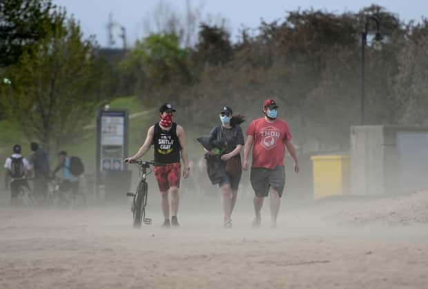 The wind blows sand into the air as three masked beachgoers take in the warm weather at Mooney's Bay beach in Ottawa May 15, 2021.