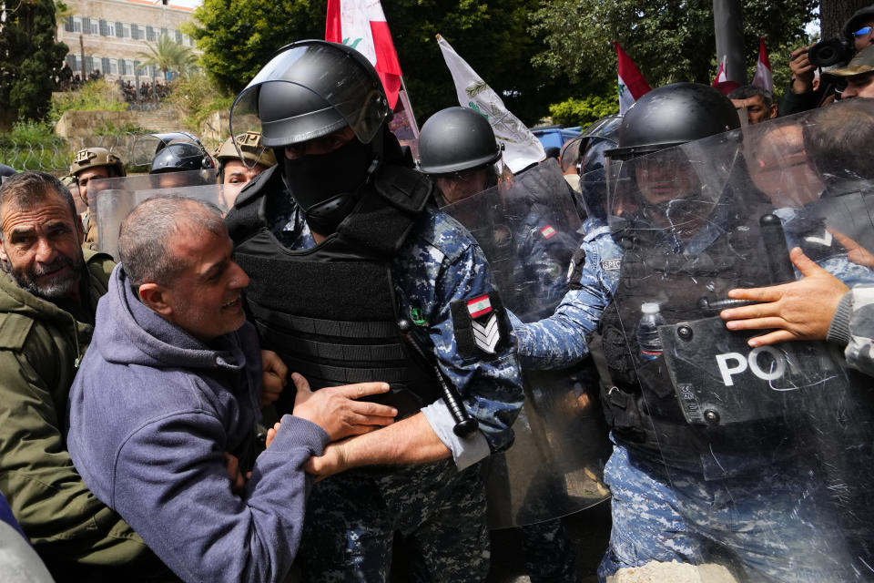 Riot police scuffle with retired members of the Lebanese security and other protesters that try to remove barbed-wire barrier and a gate in order to advance towards the government building, background, during a protest demanding better pay in Beirut, Lebanon, Wednesday, March 22, 2023. Lebanese security forces fired tear gas to disperse hundreds of protesters who tried to break through the fence leading to the government headquarters in downtown Beirut Wednesday amid widespread anger over the harsh economic conditions in the country. (AP Photo/Hassan Ammar)