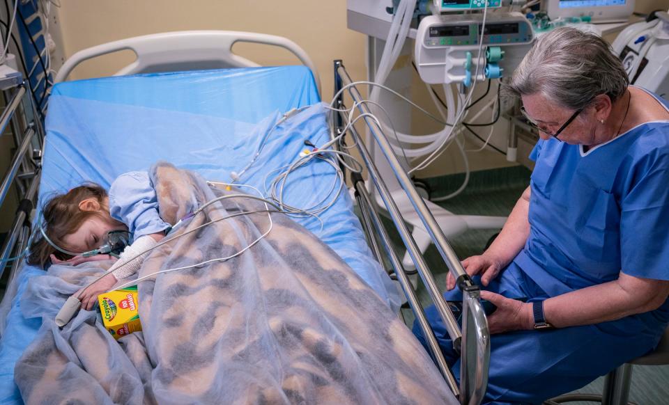 Evheniia Ukhvatova, 6, of Dnipro, Ukraine, left, rests in the recovery room at the Independent Public Health Care Facility in Leczna, Poland on Monday, May 15, 2023 as her great grandmother Valentina Ukhvatova, 75, updates family on her mobile phone about her laser surgery and skin grafts to treat burns she sustained on the back of her legs and feet in a house fire in 2020.