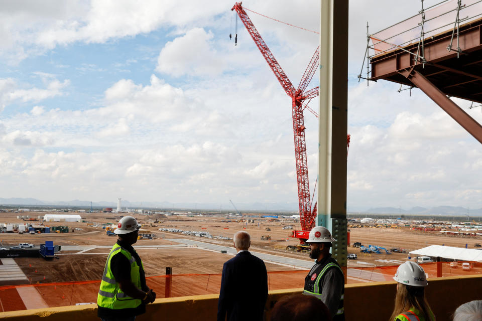 U.S. President Joe Biden looks over the site for a new semiconductor plant alongside construction workers.