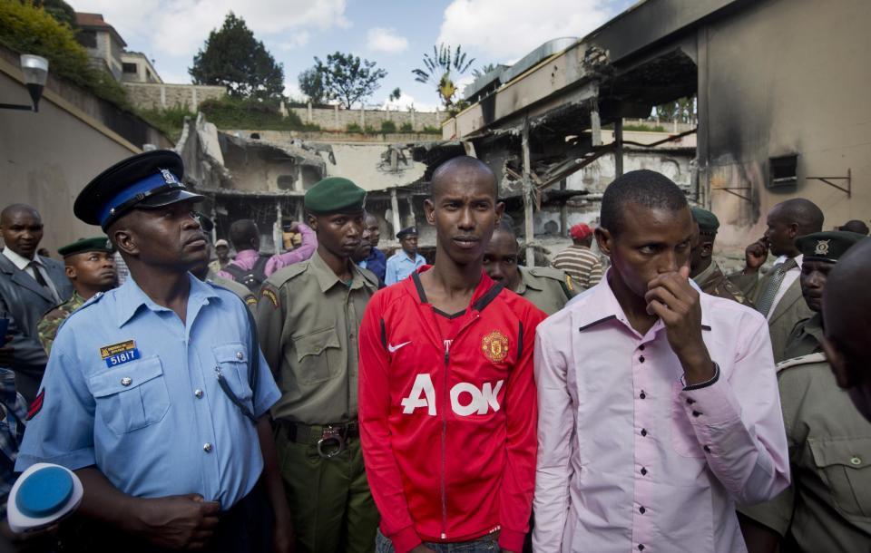 Ethnic Somalis Liban Abdullah Omar, center, and Mohamed Ahmed Abdi, center-right, who are accused of aiding the Westgate Mall gunmen, are escorted by police around the mall in Nairobi, Kenya Tuesday, Jan. 21, 2014. Court officials and four handcuffed ethnic Somalis accused of aiding the gunmen who attacked Nairobi's Westgate Mall in Sept. 2013, walked through the heavily damaged shopping center on Tuesday led by Chief Magistrate Daniel Ochenja, to help the court visualize the mall's layout for the ongoing trial of the four men. (AP Photo/Ben Curtis)