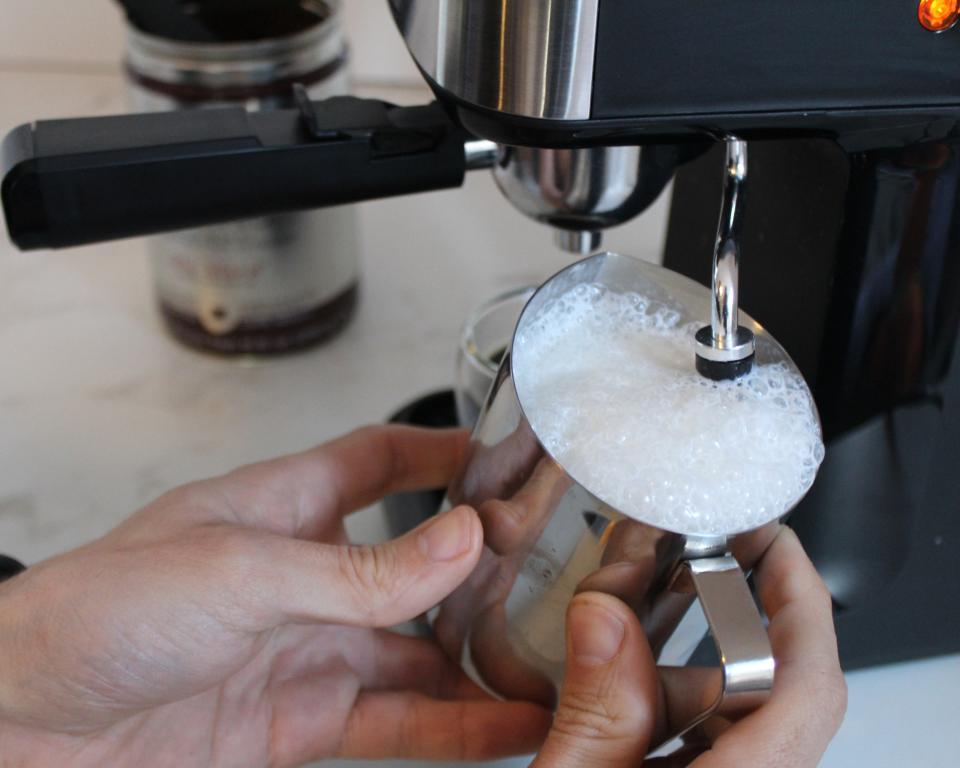 Contributing editor, Camryn Rabideau (a caucasian woman) frothing milk in stainless steel metal pitcher using the Mr. Coffee Steam Espresso Maker