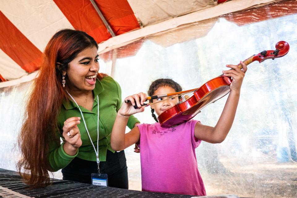 Oct 15, 2022; Northport, AL, USA; Volunteer Zumanah Kamal helps Evie Jones play at violin at the Instrument Petting Zoo during the Kentuck Festival of the Arts Saturday, Oct. 15, 2022.