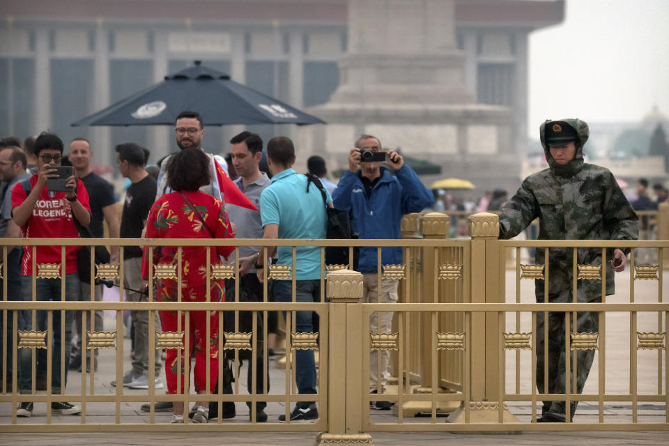 A Chinese paramilitary policeman pulls a gate closed as tourists take photos on Tiananmen Square in Beijing, Tuesday, June 4, 2019. Chinese authorities stepped up security Tuesday around Tiananmen Square in central Beijing, a reminder of the government's attempts to quash any memories of a bloody crackdown on pro-democracy protests 30 years ago. (AP Photo/Mark Schiefelbein)