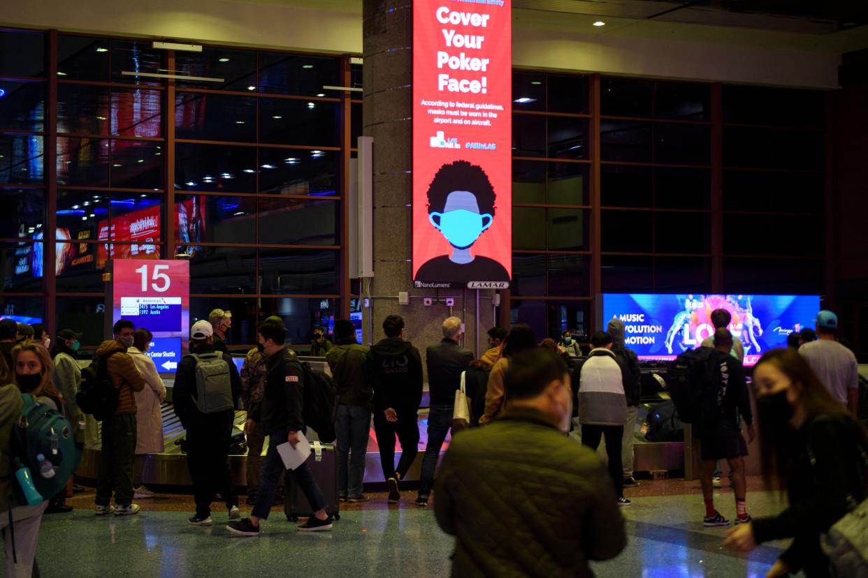 A sign reminds airline passengers to wear face masks as they wait to collect bags from a baggage carousel at the Harry Reid International Airport (LAS) in Paradise, Nevada on January 2, 2022.