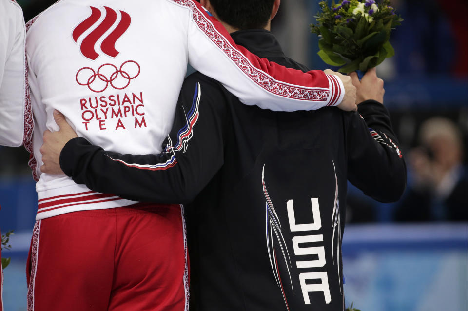 A U.S. and Russian athlete embrace as they stand on the podium during the flower ceremony for the men's 5000m short track speedskating relay final at the Iceberg Skating Palace during the 2014 Winter Olympics, Friday, Feb. 21, 2014, in Sochi, Russia. Russia finished first, followed by the United States and China. (AP Photo/Bernat Armangue)