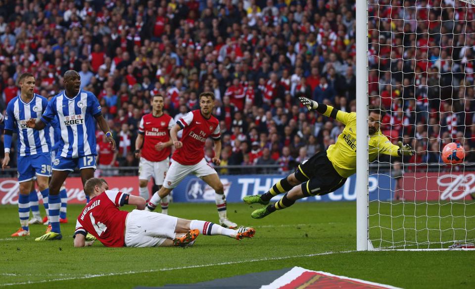 Arsenal's Per Mertesacker (4, bottom) heads and scores his goal against Wigan Athletic during their English FA Cup semi-final soccer match at Wembley Stadium in London April 12, 2014. REUTERS/Eddie Keogh (BRITAIN - Tags: SPORT SOCCER TPX IMAGES OF THE DAY)