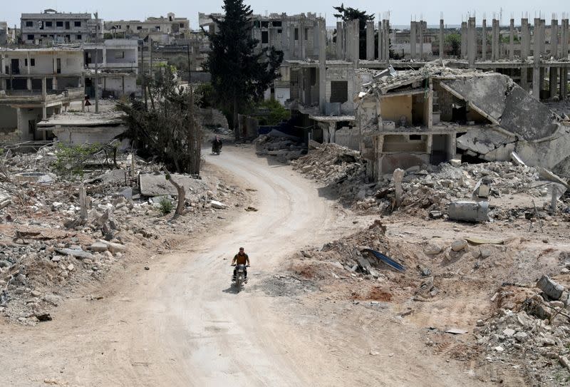 FILE PHOTO: A man rides a motorbike past damaged buildings in the rebel-held town of Nairab