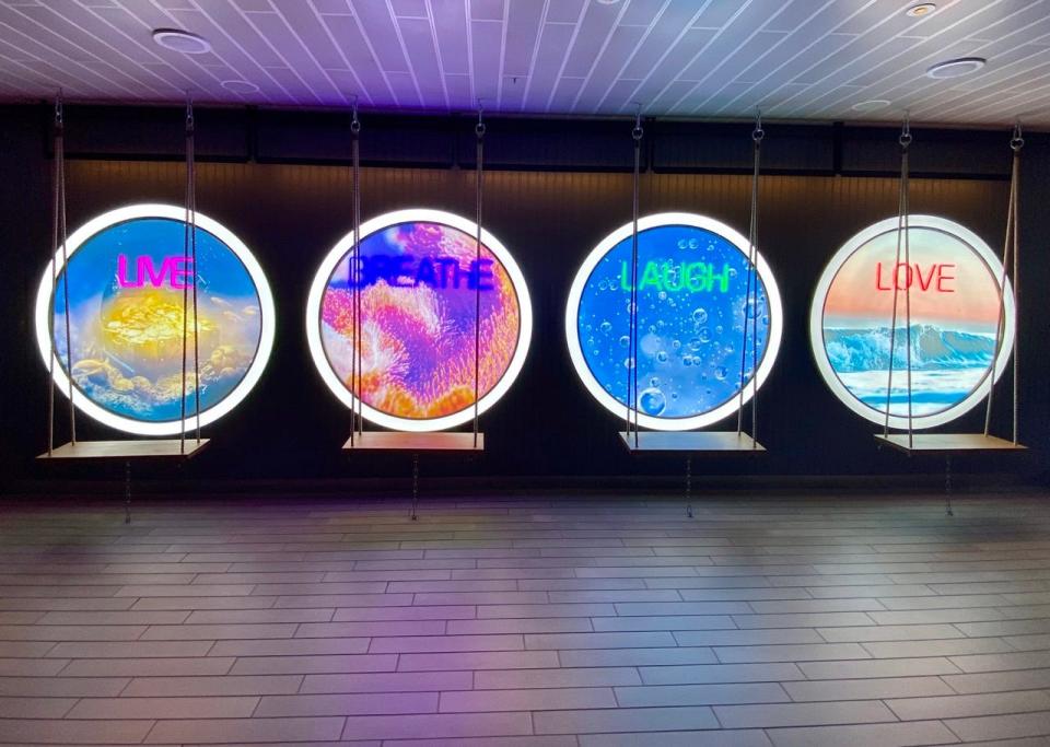 Swings in front of neon-lit porthole circles on Virgin Voyages Scarlet Lady