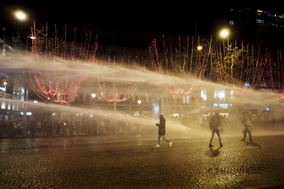 Demonstrators wearing yellow vests are blasted with a police water canon on the Champs Elysees avenue in Paris Saturday, Dec. 22, 2018. France's yellow vest protesters, who have brought chaos to Paris over the past few weeks with their economic demands, demonstrated in sharply reduced numbers Saturday at the start of the Christmas and New Year holidays. (AP Photo/Kamil Zihnioglu)