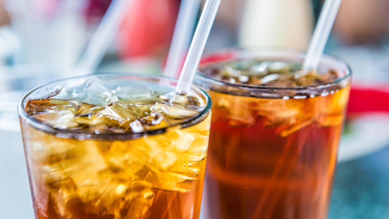 Macro closeup of iced tea or soda with ice cubes and straw in glass.