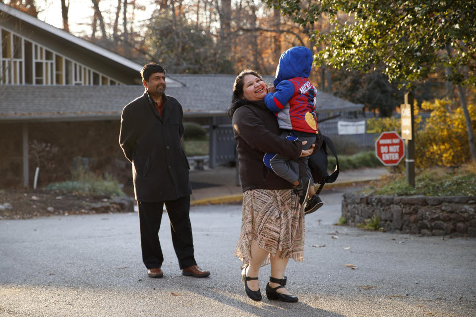 Rev. Abhi Janamanchi, left, watches as holds Rosa Gutierrez Lopez picks up her son John, 7, who has Down syndrome, after John arrived on the school bus to Cedar Lane Unitarian Universalist Church where the Gutierrez Lopez family is living, in Bethesda, Md., Thursday, Dec. 5, 2019. Gutierrez Lopez, who a year ago became the first unauthorized immigrant to get refuge inside a religious institution in the Washington area, has now been living in sanctuary for a year due to a deportation order. (AP Photo/Jacquelyn Martin)