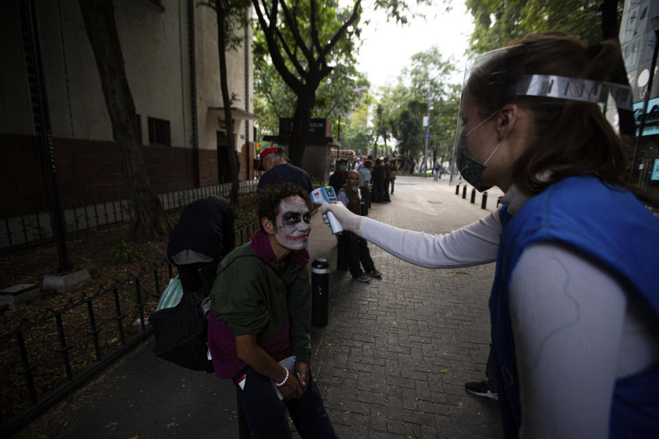 A volunteer takes the temperature of a homeless man with his face painted, screening for COVID-19 symptoms at a line to receive a free meal in Mexico City, Wednesday, May 20, 2020. The volunteers running the soup kitchen say they have had to expand their service from a single day to two days per week as the number of people in need grows. (AP Photo/Fernando Llano)