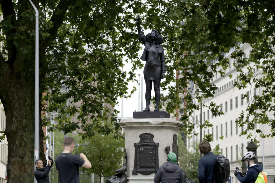 People use their phones to document a new black resin and steel statue entitled "A Surge of Power (Jen Reid) 2020" by artist Marc Quinn after it was put up this morning on the empty plinth of the toppled statue of 17th century slave trader Edward Colston, which was pulled down during a Black Lives Matter protest in Bristol, England, Wednesday, July 15, 2020. On June 7 anti-racism demonstrators pulled the 18-foot (5.5 meter) bronze likeness of Colston down, dragged it to the nearby harbor and dumped it in the River Avon — sparking both delight and dismay in Britain and beyond. (AP Photo/Matt Dunham)