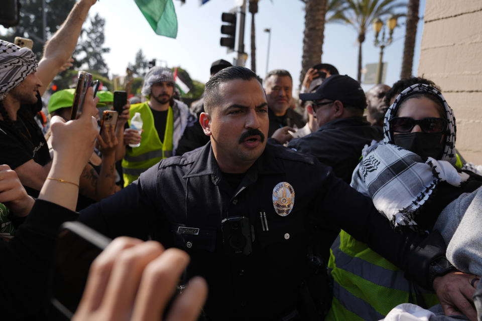A Los Angeles Police Department officer attempts to make a hole where pro-Palestinian demonstrators were attempting to keep attendees from getting through at the Shrine Auditorium where a commencement ceremony for graduates from Pomona College was being held, Sunday, May 12, 2024, in Los Angeles. (AP Photo/Ryan Sun)