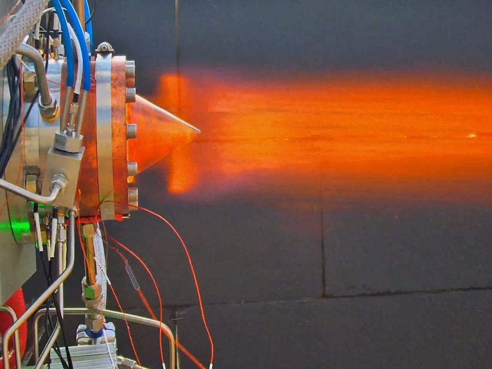 An orange flame coming out the back of a jet engine with exposed wiring.