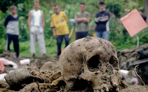Bosnian Muslim villagers look at the remains of bodies exhumed from a mass grave in the village of Kamenica, Bosnia - Credit: Amel Emric/AP