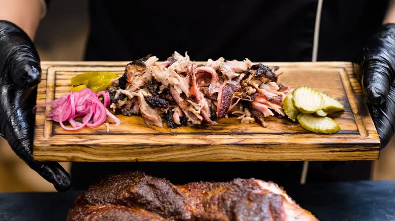 Hands holding a tray with shredded pork and pickles