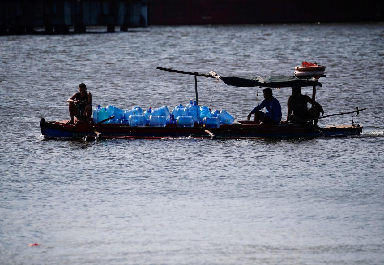 Fishermen on a boat carry containers with potable water in Manila (EPA)