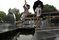 A child leaps across a water feature during a rainy day in Beijing, Sunday, Aug. 14, 2022. (AP Photo/Ng Han Guan)