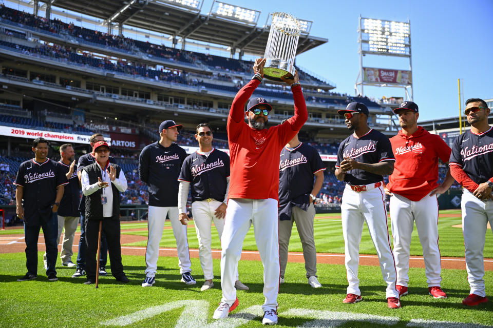 Washington Nationals manager Dave Martinez, center, holds up the 2019 World Series trophy during a pre-game ceremony to celebrate the five year anniversary of the Nationals win over the Houston Astros in the 2019 World Series before a baseball game between the two teams at Nationals Park, Saturday, April 20, 2024, in Washington. (AP Photo/John McDonnell)