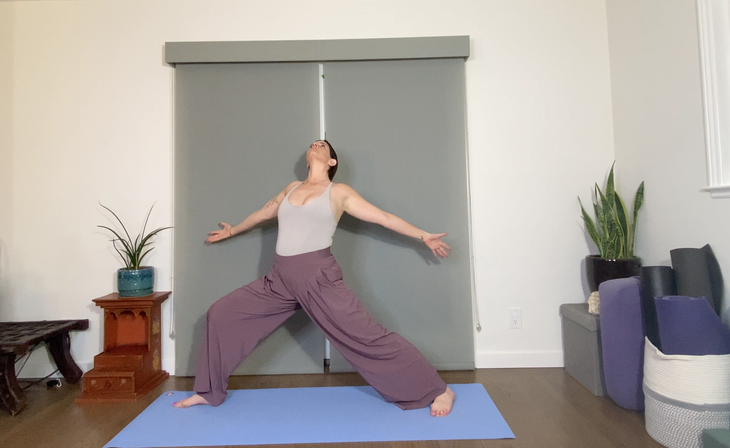 A woman wearing loose purple pants and a gray tank practice a variation of Warrior 2 Pose