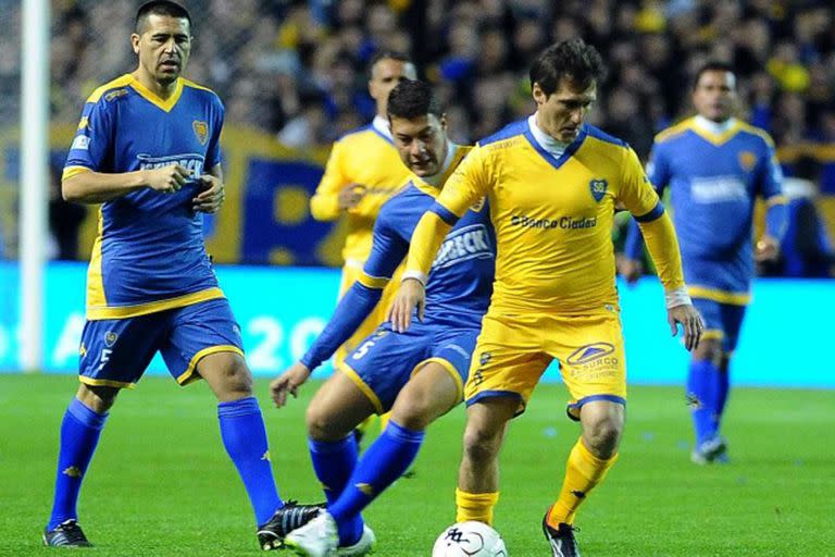 Battaglia marca a Guillermo Barros Schelotto, en su partido homenaje de 2015, cerca suyo, Juan Román Riquelme