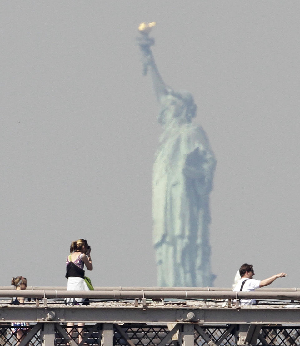 FILE - In this May 1, 2010 file photo, the Statue of Liberty appears in the distance as a woman stops to take photos on the Brooklyn Bridge in New York. The Statue of Liberty, which has been closed to visitors since Superstorm Sandy, is scheduled to reopen for tours July Fourth, when Statue Cruises resumes departures for Liberty Island from Lower Manhattan. For tourists who want a photo of the famous statue without visiting the island, there are many options and vantage points, including a view from a walk over the Brooklyn Bridge. (AP Photo/Peter Morgan, file)