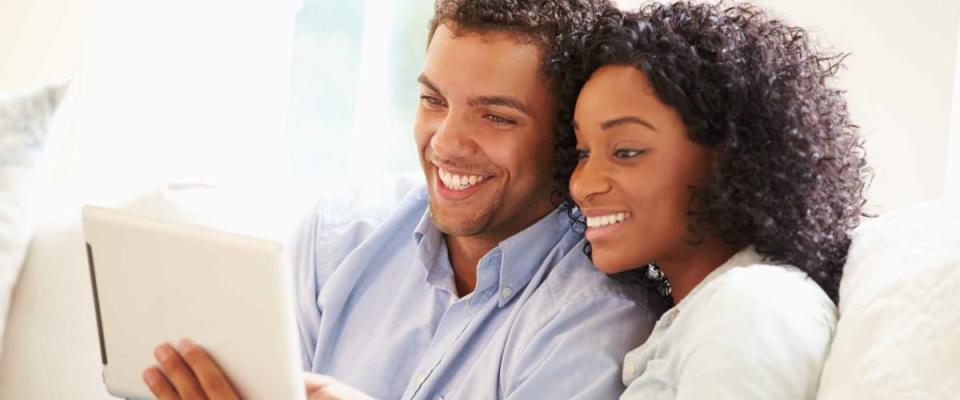 Young Couple Sitting On Sofa Using Digital Tablet