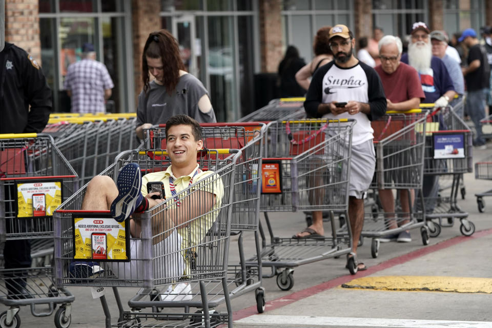 John Sinoski sits in a shopping cart while waiting for an H-E-B grocery store to open Tuesday, March 17, 2020, in Spring, Texas. Sinoski, who arrived around 6:30 in the morning, was near the front of a line of more than 150 people waiting to enter the store which opened at 8:00 a.m. Grocery store executives and city officials reassured the community, on Monday, that plenty of food will be available in their stores and urged people not to stockpile groceries amid coronavirus concerns. (AP Photo/David J. Phillip)