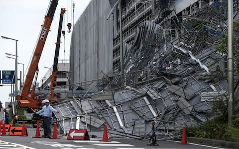 Workers direct traffic in front of damaged scaffolding at the construction site of a parking garage at Haneda Airport - Credit: Getty