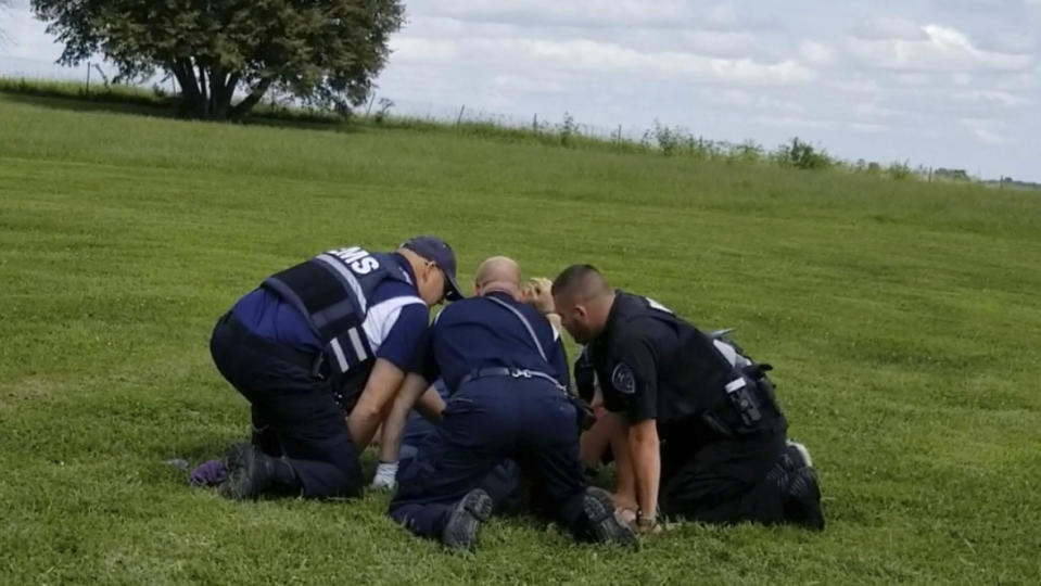 In this image from video provided by a family friend, Taylor Ware is restrained by law enforcement and emergency medical personnel at a highway rest stop in Dale, Ind., on Aug. 25, 2019. Taylor's mother called 911 when he wouldn’t get back in their SUV during a manic episode caused by bipolar disorder. A cascade of force ended with Ware in a coma. He died three days later. (Pauline Engel via AP)